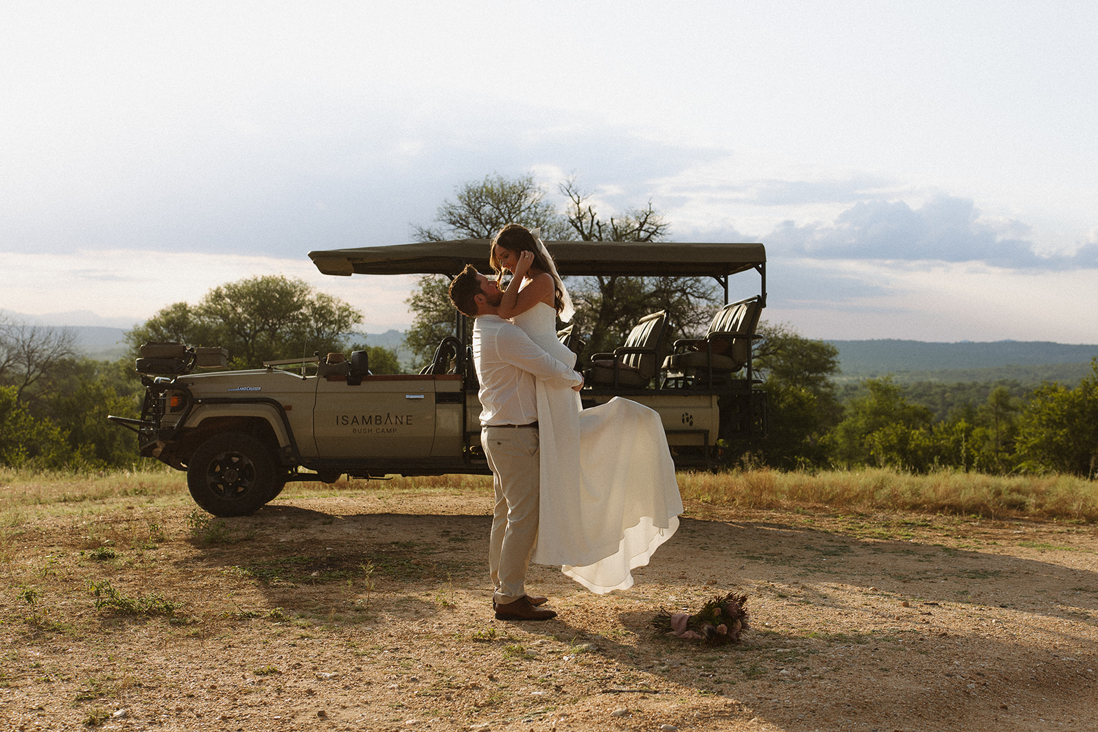 Groom lifting bride in front of safari vehicle with bouquet on the ground during a romantic safari wedding packages moment
