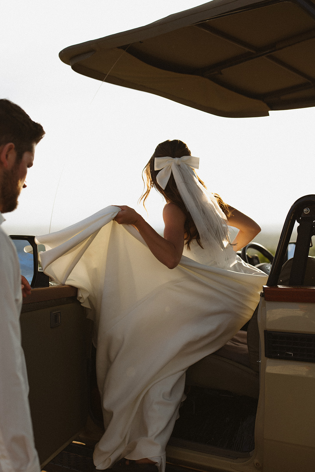 Bride climbing into safari vehicle with flowing dress and veil during a golden hour safari wedding moment