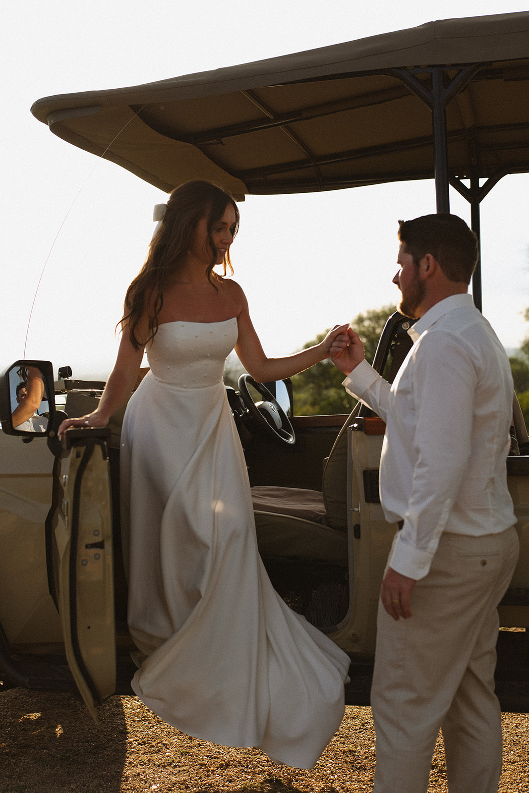 Bride stepping out of safari jeep holding groom’s hand in warm sunset light during a safari wedding packages experience
