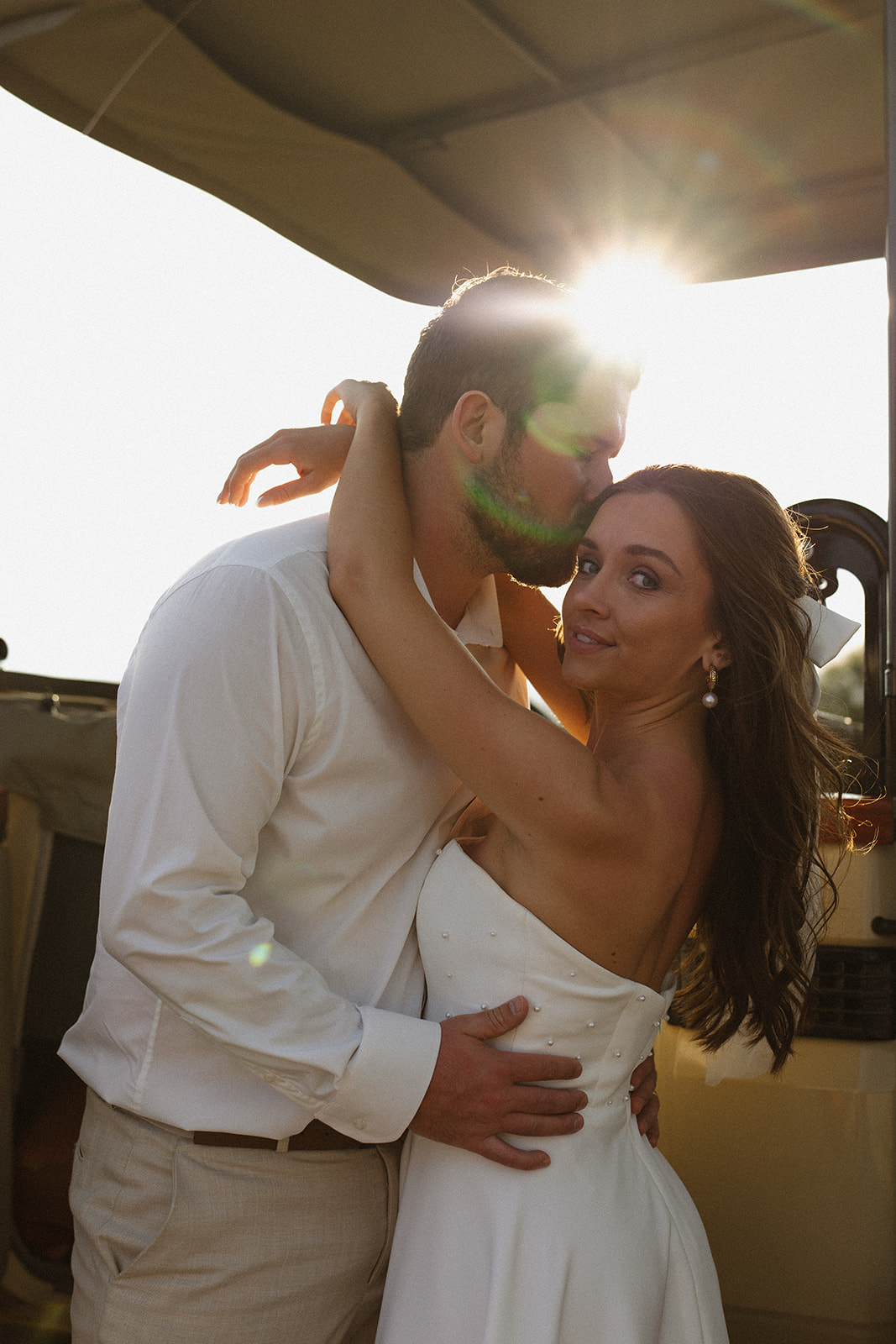 Bride and groom embracing closely on safari jeep with sun flare and romantic golden hour lighting during a safari wedding packages experience
