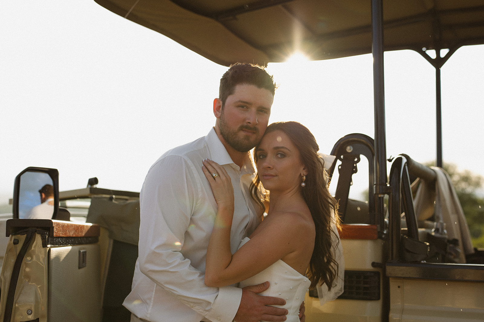 Bride and groom posing together on safari jeep with warm backlight and scenic views during their wedding day
