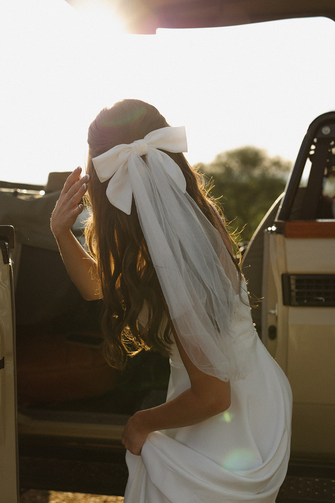 Bride stepping into safari vehicle with veil and bow glowing in golden light during a safari wedding packages adventure
