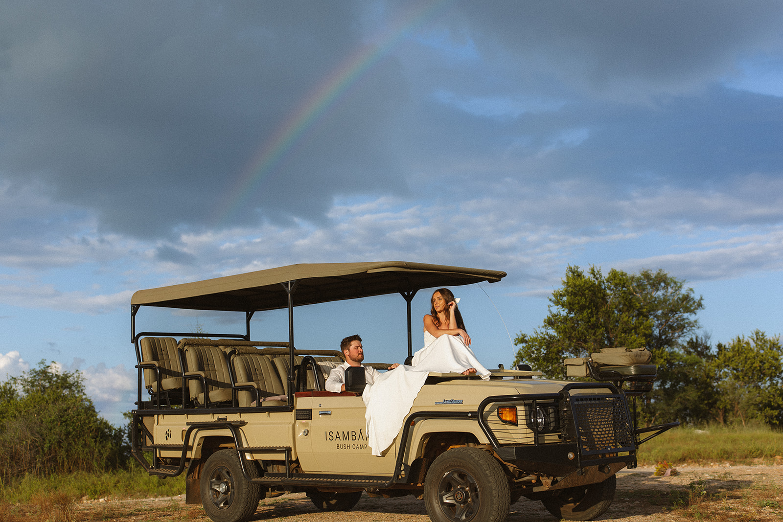 Bride sitting on safari vehicle under a rainbow in the African sky during a unique safari wedding packages moment
