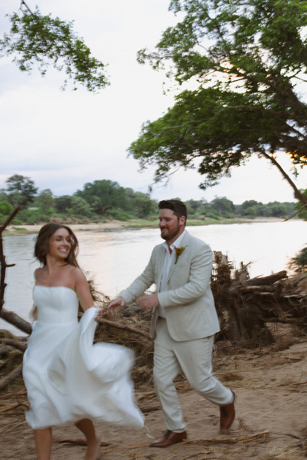 Bride and groom running playfully along sandy riverbank during a joyful safari wedding packages moment
