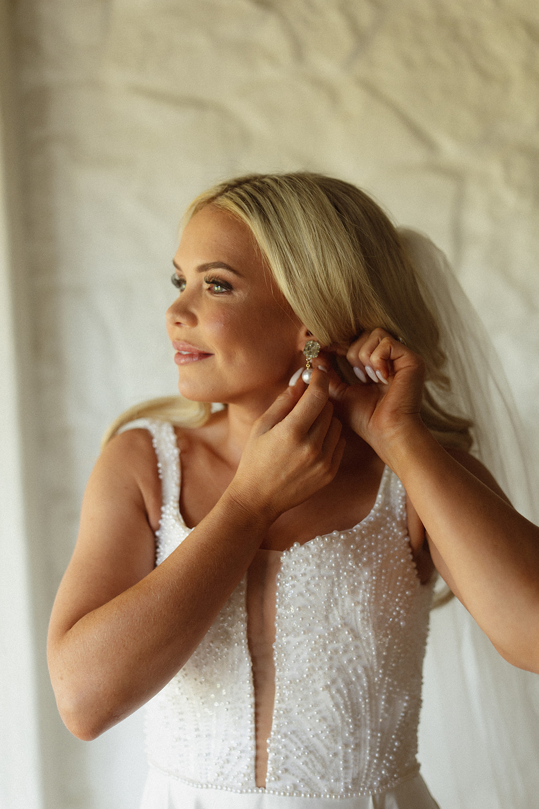 Bride putting on earrings in soft natural light during wedding morning at a safari lodge