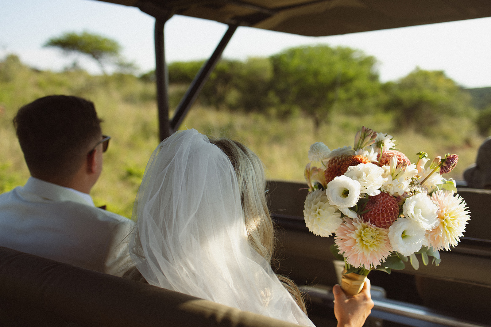 Bride and groom riding in safari vehicle with bouquet during a safari wedding in South Africa