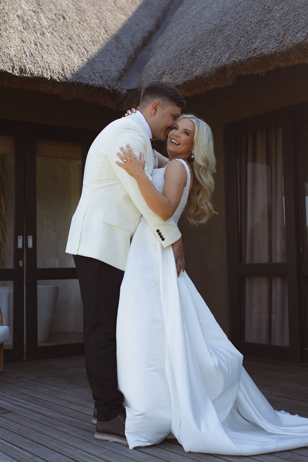 Bride and groom embracing outside a thatched safari lodge during their wedding day in South Africa