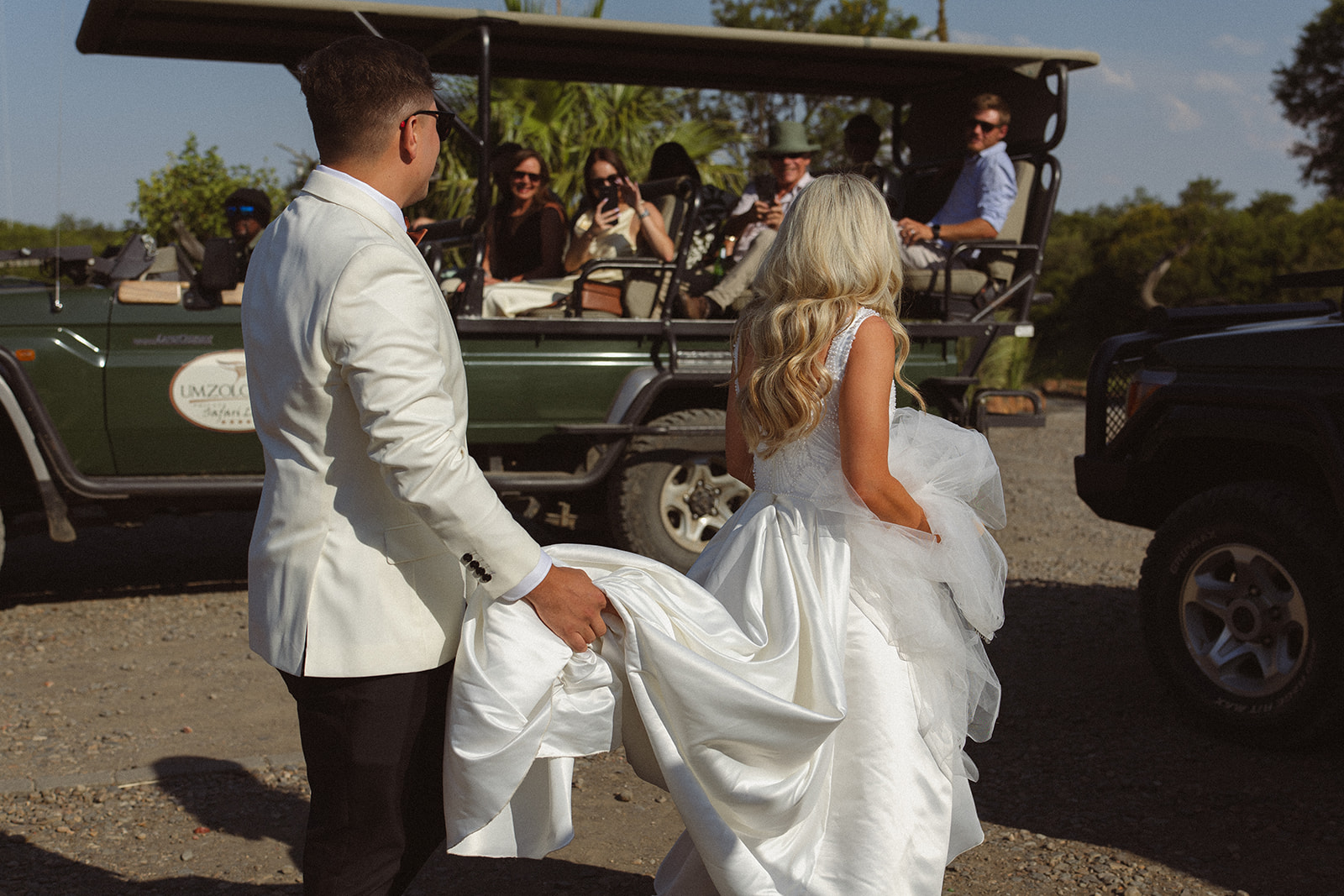Bride and groom walking toward safari vehicle with guests during wedding day in South Africa