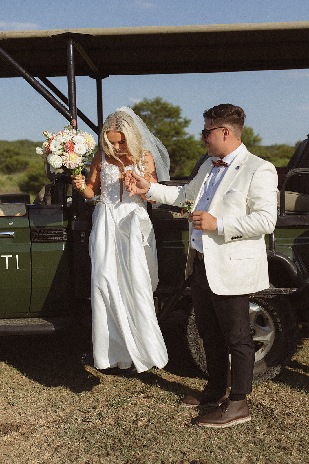 Bride stepping out of safari vehicle with groom helping her during a safari wedding in South Africa