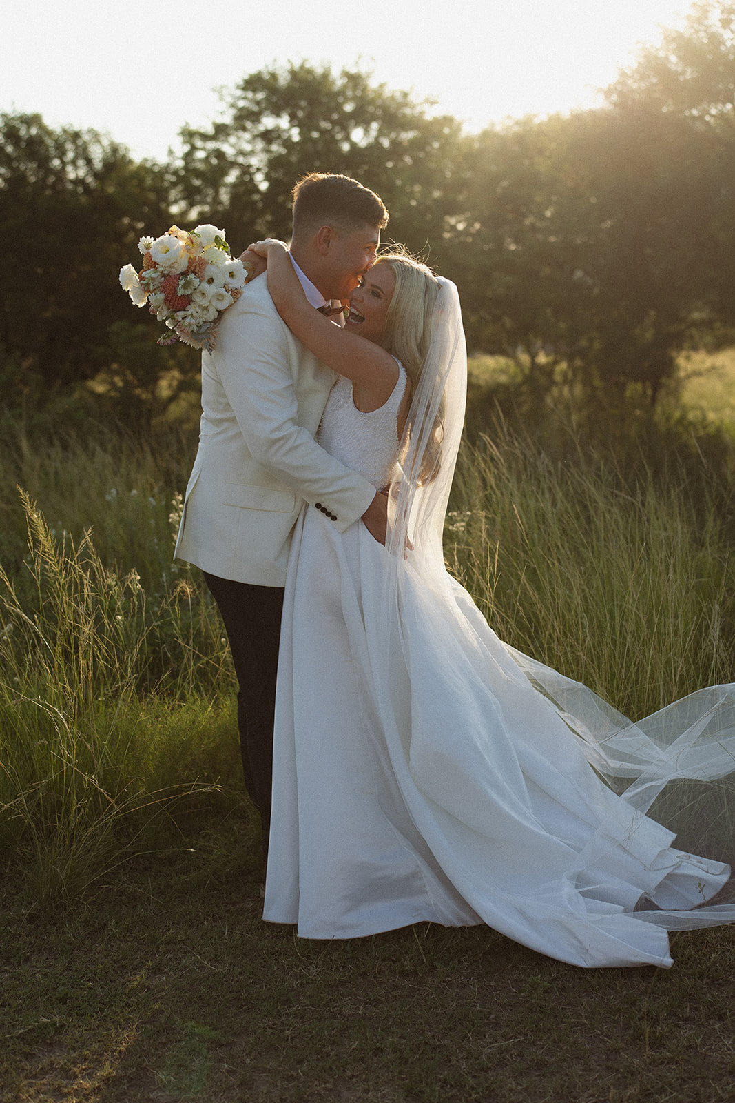 Bride and groom embracing with flowing veil in open landscape during South Africa wedding