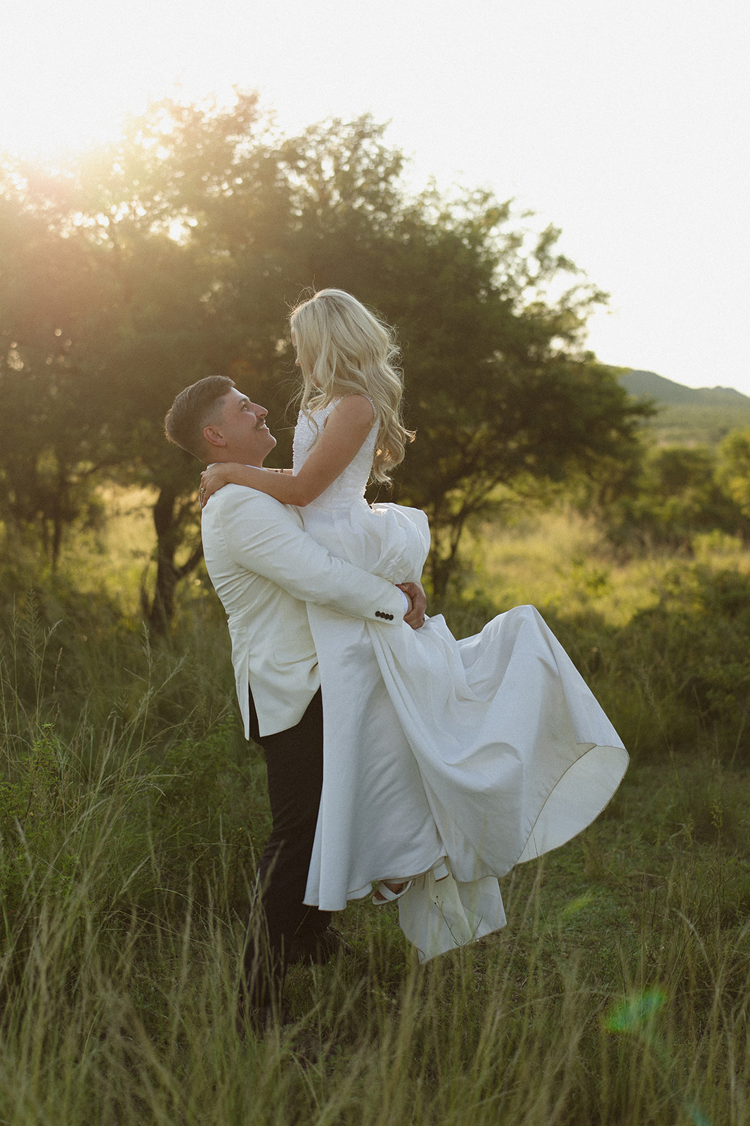 Groom lifting bride in tall grass during golden hour in South Africa