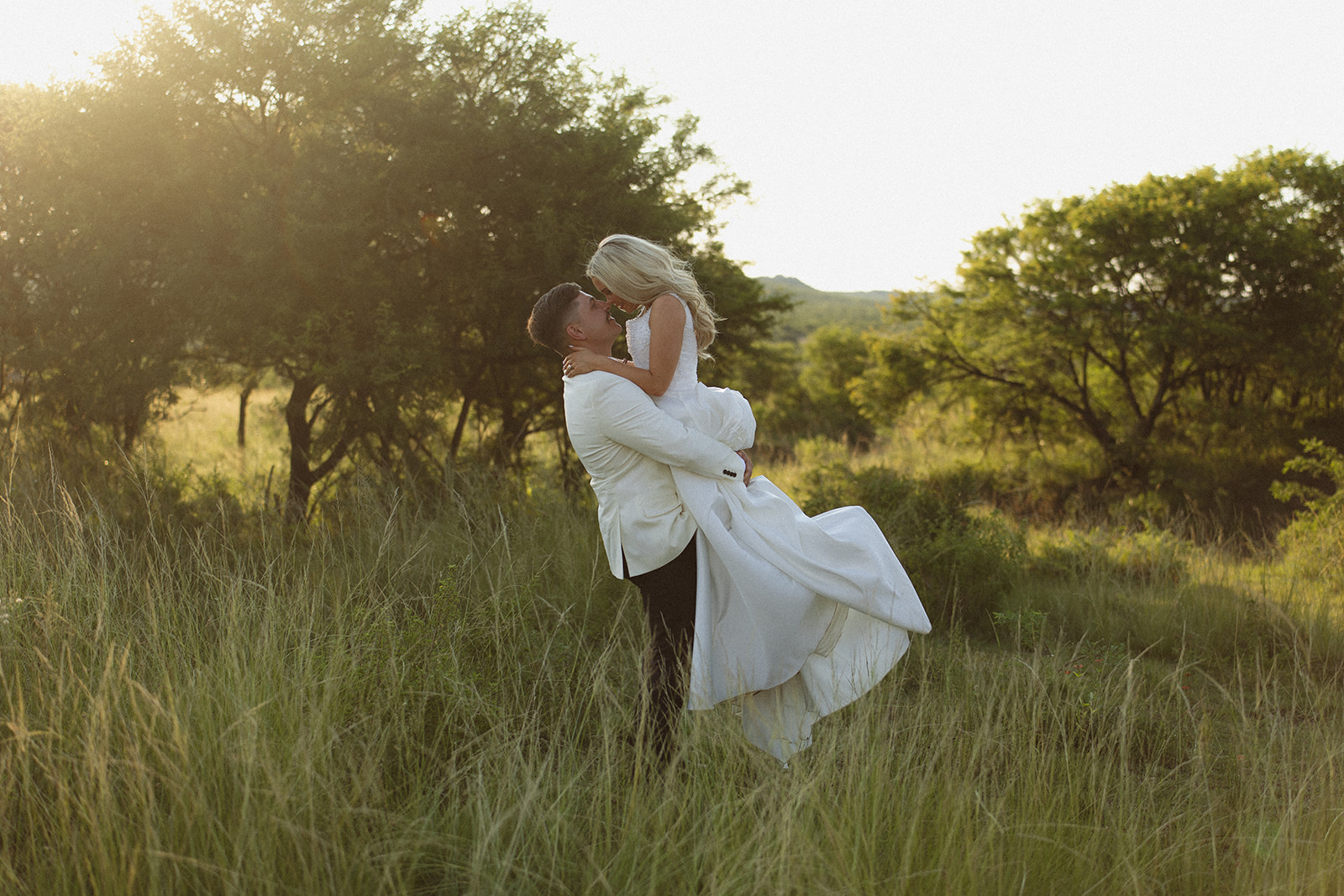 Groom lifting bride in tall grass during golden hour at a safari wedding in South Africa