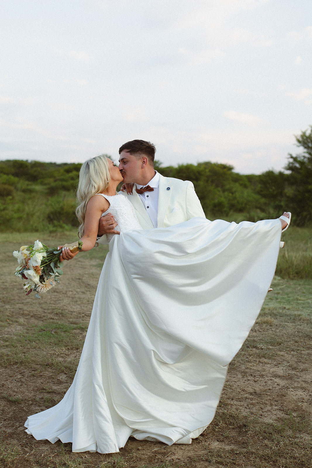 Groom dipping bride for a kiss in open field during wedding day in South Africa