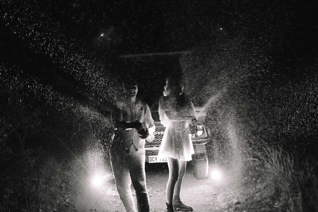 Sorica and Caleb spraying champagne beside their safari vehicle at night during their Lion Sands elopement
