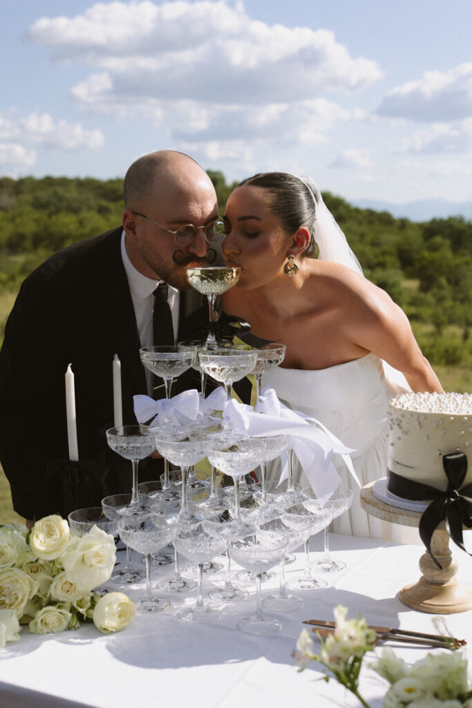 Bride and groom sharing champagne from a tower during their intimate safari wedding celebration