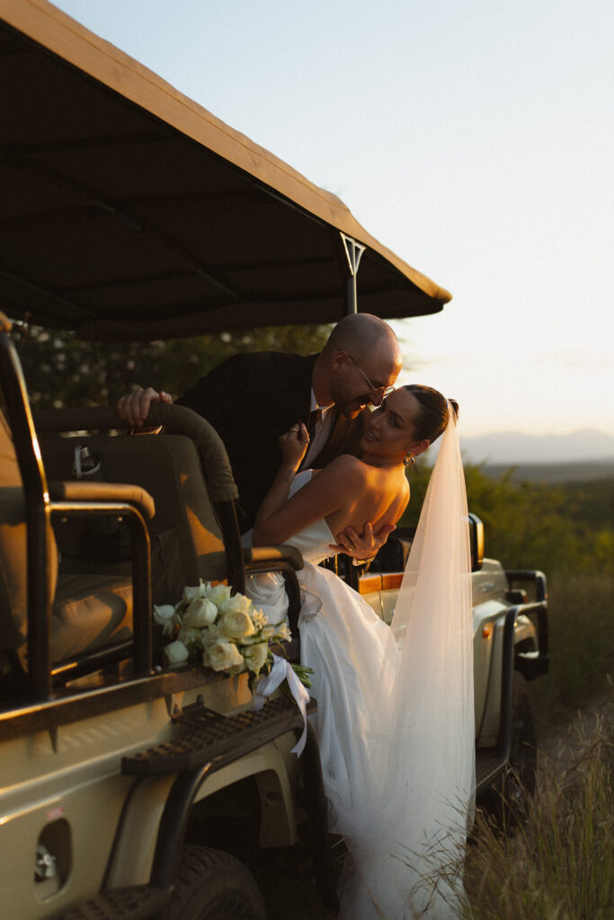 Bride and groom sharing a moment beside a safari vehicle at sunset during their South Africa elopement